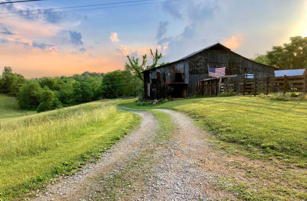 dirt road leading to a dilapidated barn with an American flag