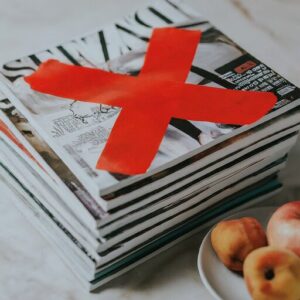 a stack of glossy magazines with a red X representing what not to compost